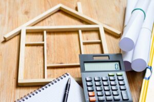 Rental remodel checklist is represented by planning tools like a calculator, pencil, and pad of paper around the structure of a rental home